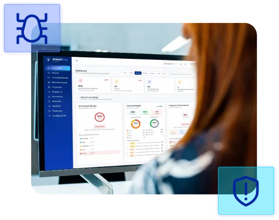 Monitor con el dashboard de ShieldOne y persona del equipo revisándolo, con iconos de vulnerabilidad y protección superpuestos